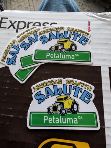 Customer's custom vinyl stickers with an 'American Graffiti Salute' design fanned out on a box.