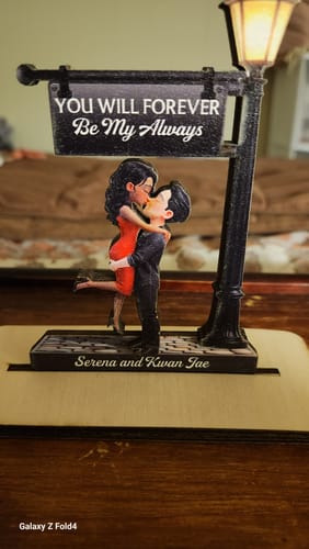 Customer's personalized wooden plaque showing a couple kissing under a lit lamppost, with custom names on the base.