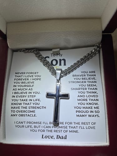 Customer's artisan cross on a Cuban link chain resting on the message card inside its red gift box.