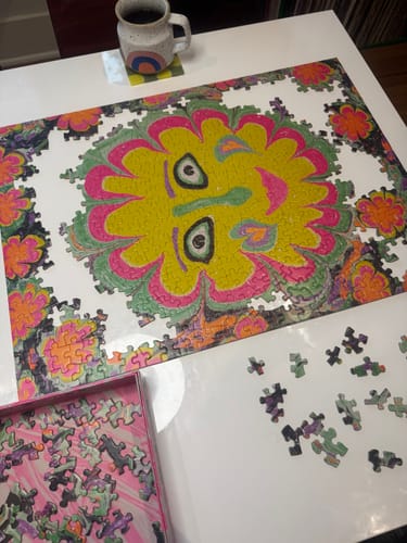 Customer's nearly completed Freaky Deaky Puzzle on a white table, showing its colorful, psychedelic design with a smiling face.