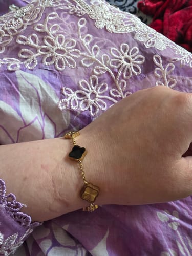 Reviewer wearing the Celine Clover Bracelet on their wrist, showing the black enamel and textured gold clovers.