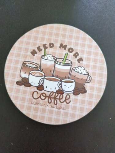 Close-up of a reviewer's cute coaster from the Coffee Lovers Box Set, featuring a 'Need More Coffee' graphic.