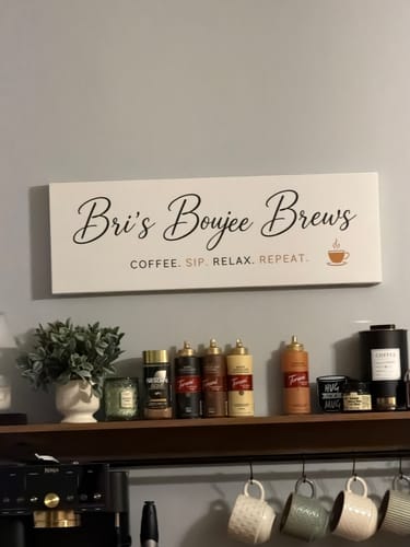 Rezensent zeigt ein individuelles, weißes Schild mit der Aufschrift "Bri's Boujee Brews", das über einer Kaffeestation hängt.