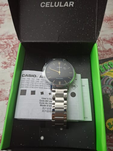 Cliente muestra su reloj Casio análogo con pulsera metálica y esfera negra dentro de su caja.