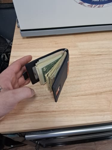 Reviewer holding the matte black leather wallet open, showing it packed with cash.