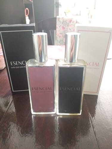 Reseñador muestra dos frascos de perfume Esencial, uno rosa y uno negro, sobre una mesa de madera.