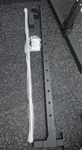 Ein Kunde zeigt die stabilen, ausgepackten Teile des R7 Smith Option Pakets 1 auf einem Fitnessboden.