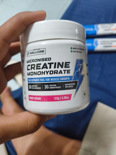 Reviewer holding the white tub of Wellcore Micronised Creatine Monohydrate, showing the front label.