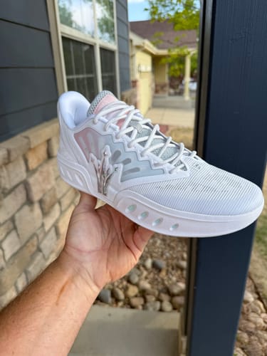 Reviewer holding the white SHUFFLE 2 "MIRO" shoe with pink accents outdoors.