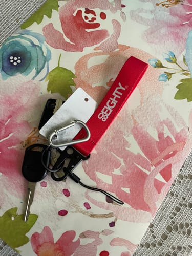 Customer's red 80Eighty WristStrap with keys and a carabiner lying on a floral surface.