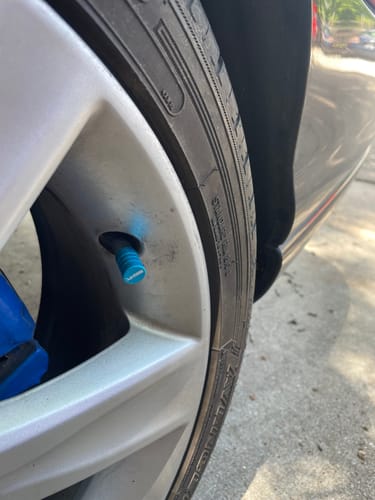 Customer's close-up of a teal valve stem cap installed on a silver car wheel.