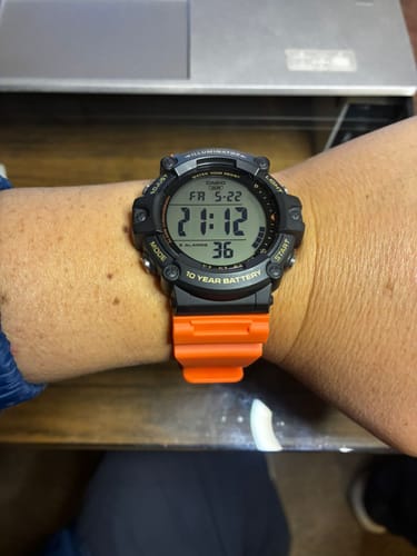 Un cliente muestra en su muñeca el Reloj Casio Vintage con la esfera negra y una correa naranja.