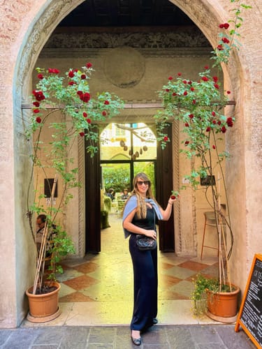 Reviewer standing in an archway wearing the long, navy Cole Satin Trousers with a black top.