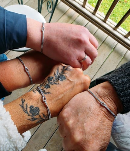 Reviewer's photo showing three friends wearing matching silver-colored knot bracelets as a gift.