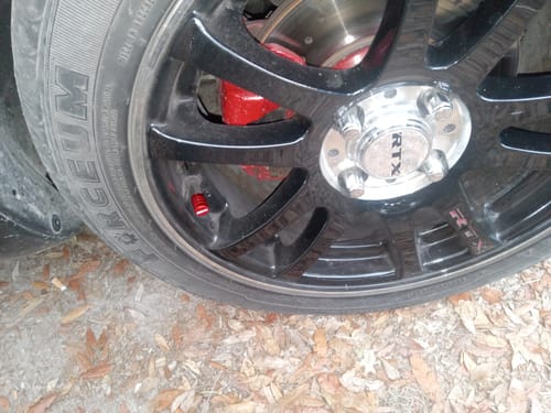 Close-up of a customer's red valve stem cap installed on a black car wheel.
