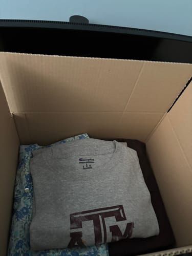 Recensore mostra la sua Fiore Vintage Box aperta, che contiene una pila di vestiti con una t-shirt grigia in cima.