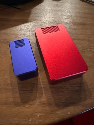 Reviewer's indigo Nano Case sitting next to a larger red case on a wooden table for comparison.