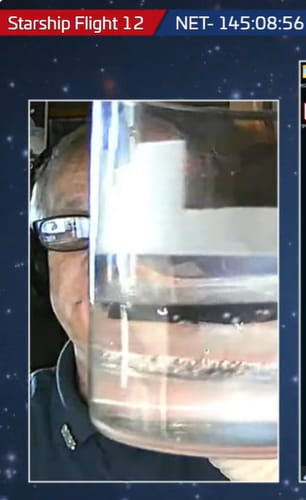 Partial view of a reviewer holding a Starbase 2025 Whiskey Glass filled with a clear, bubbly liquid.