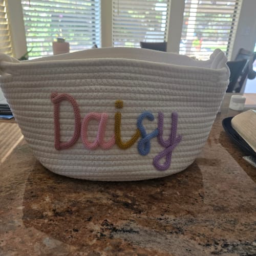 Customer's large personalized knitted basket with the name "Daisy" in colorful yarn sitting on a countertop.