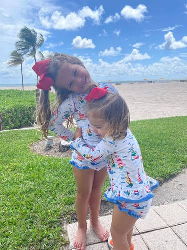 Reviewer's two children hugging in matching Watercolor Sailboat Rash Guard Sets by the beach.