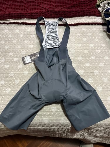 Reviewer's gray LIFTTINT 2.X BIB SHORTS laid out on a bed, showing the padded seat and striped back straps.