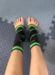 Cliente usando las tobilleras Isnovas negras con verde en ambos pies, visto desde arriba sobre un piso azul.