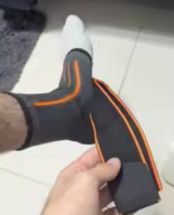 Cliente ajustando la tobillera negra Isnovas con detalles naranjas en su pie.