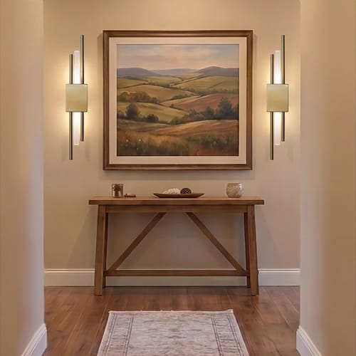 Customer's two gold Ambio Wireless Sconces lit up in a hallway, flanking a framed painting.