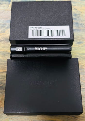 A customer's new 80Eighty® Onyx Wallet is displayed between its two black packaging boxes on a wooden surface.