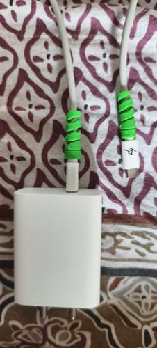 Reviewer shows two green spiral cable protectors on white cables plugged into a charging block.