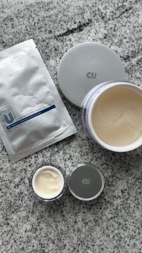Apžvalgininko CUSKIN lakštinė kaukė pakuotėje, gulinti šalia kitų tos pačios linijos produktų.