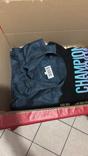 Cliente mostra il contenuto della sua scatola Fiore Vintage con una selezione di capi vintage, tra cui una camicia blu e una t-shirt.