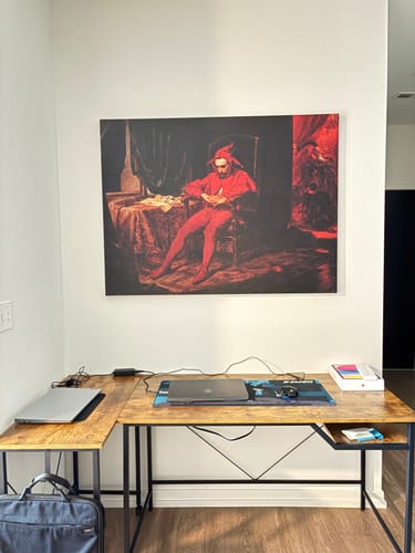 Customer's 'Stańczyk - The Sad Jester' canvas print hanging on a white wall above a wooden desk.