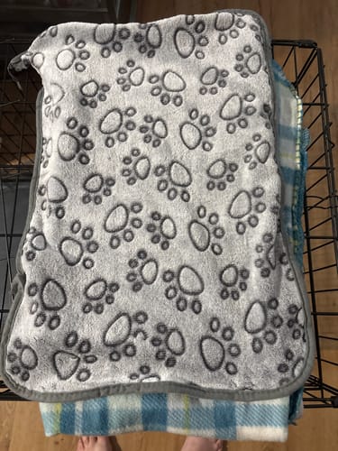 Customer's soft, grey Anti-Stress Blanket with a paw print pattern folded on a pet crate.