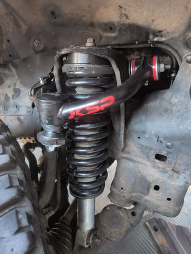 Customer's black KSP Upper Control Arms installed on their vehicle's front suspension next to the coil spring.