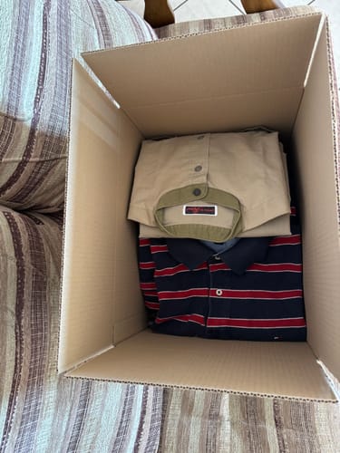 Un cliente mostra la sua box di rivendita aperta con dentro vestiti vintage piegati, come una camicia e una polo.