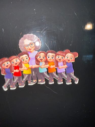 Customer's personalized acrylic magnet showing a cartoon grandma and a line of seven grandkids on a dark refrigerator.