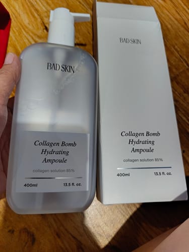 Customer holds the large Bad Skin Collagen Bomb Hydrating Ampoule bottle next to its white product box.