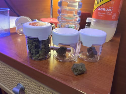 Reviewer's jars of Golden Mousse on a wooden table, displayed next to a jar of another cannabis product.