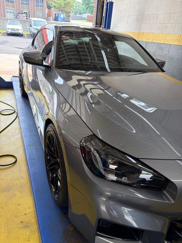 Customer's grey BMW on a car lift, showing the front wheel's improved stance after installing the Wheel Spacers.