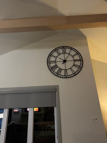 Customer's large black Roman numeral wall clock mounted high on a light-colored wall in a room.