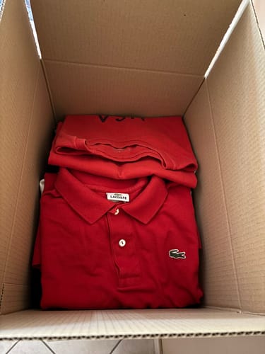 Cliente mostra il contenuto della scatola per la rivendita con una polo rossa piegata in cima.