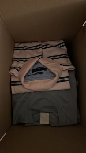 Recensore mostra i vestiti piegati all'interno della scatola Fiore Vintage, tra cui una polo a righe.