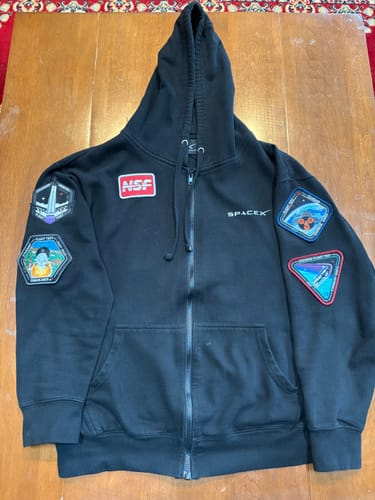 Reviewer's black zip-up hoodie showing several collector's patches on the front and sleeves.