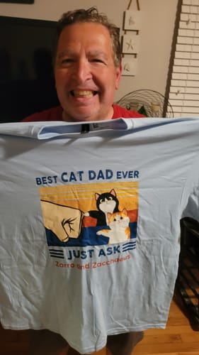 Customer holding up a light blue personalized 'Best Cat Dad Ever' shirt with a cat fist bump graphic.