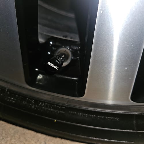 Close-up of a reviewer's black 80Eighty® Valve Stem Cap installed on a car wheel.