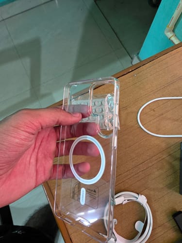 Reviewer holding a clear phone case with a white magnetic ring over a wooden desk.