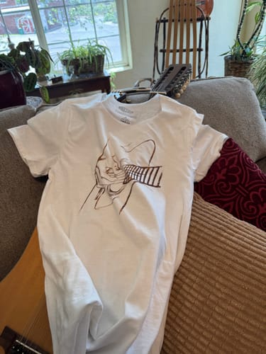Reviewer's white Golden Strings T-Shirt with a line-art graphic laid out on a couch.