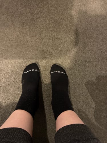 A reviewer's feet in the warm black Ankle Socks, viewed from above on a carpeted floor.