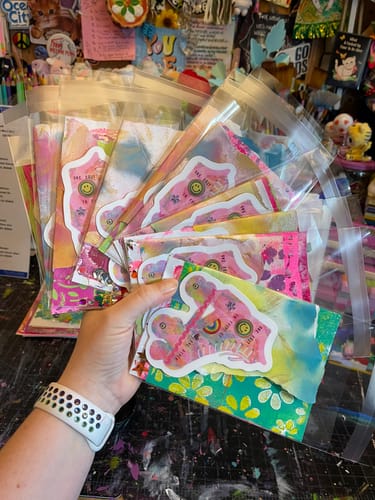 Reviewer holding multiple clear bags of custom, colorful vinyl stickers.